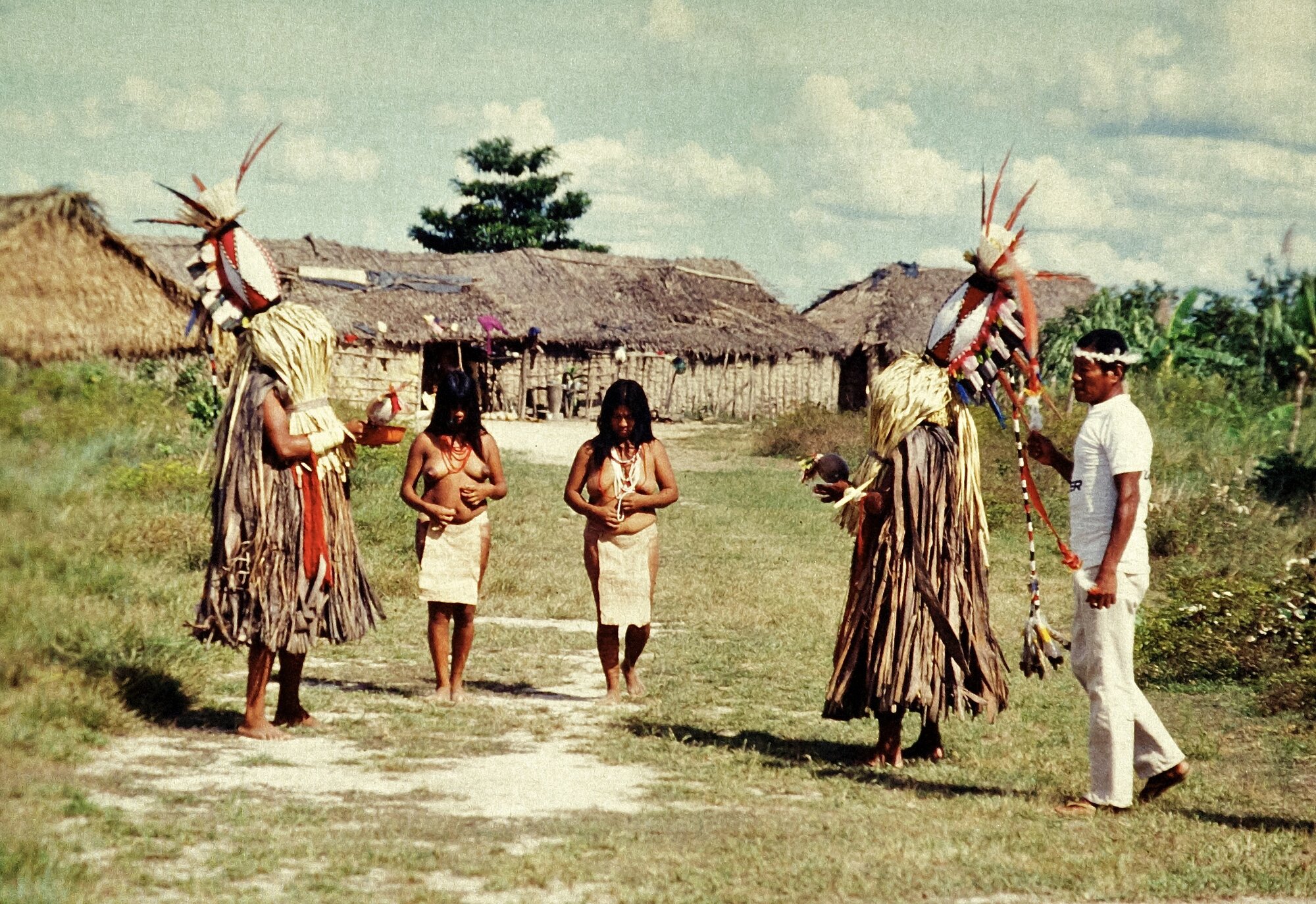 Karajá ceremonial scene with dancers in traditional straw costumes and feathered headdresses in a village