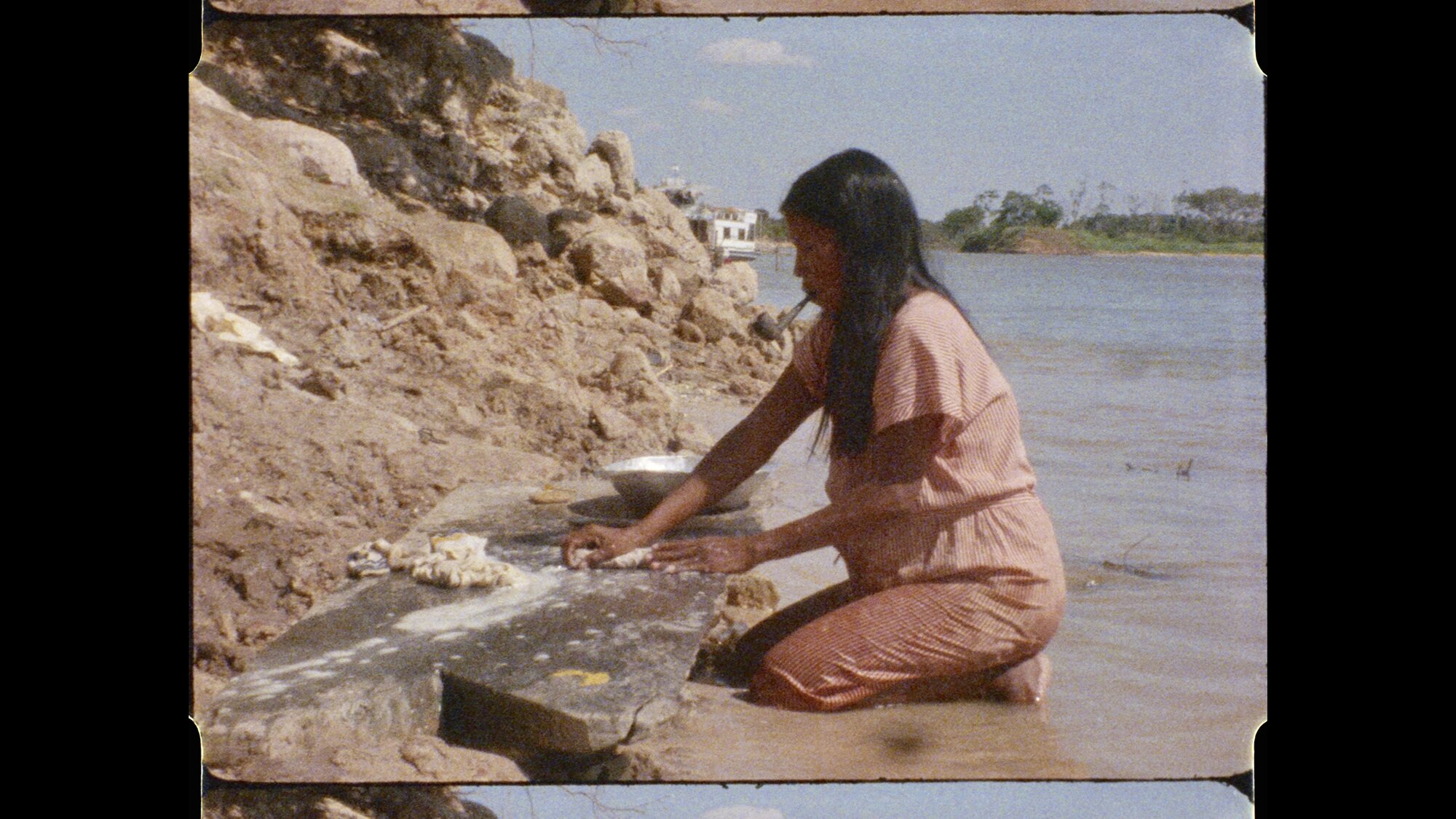 Diriti in pink clothing kneeling by the Araguaia riverbank, working with clay
