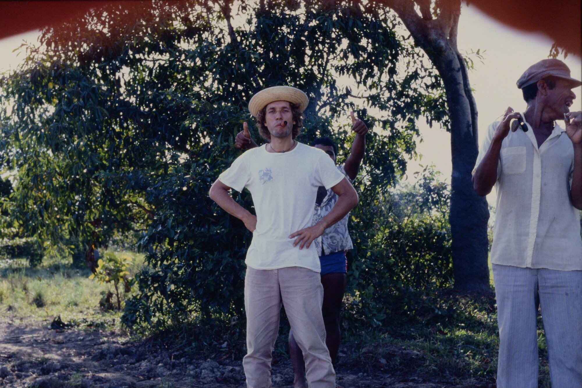 Young Matti in a straw hat and white t-shirt standing with locals outdoors
