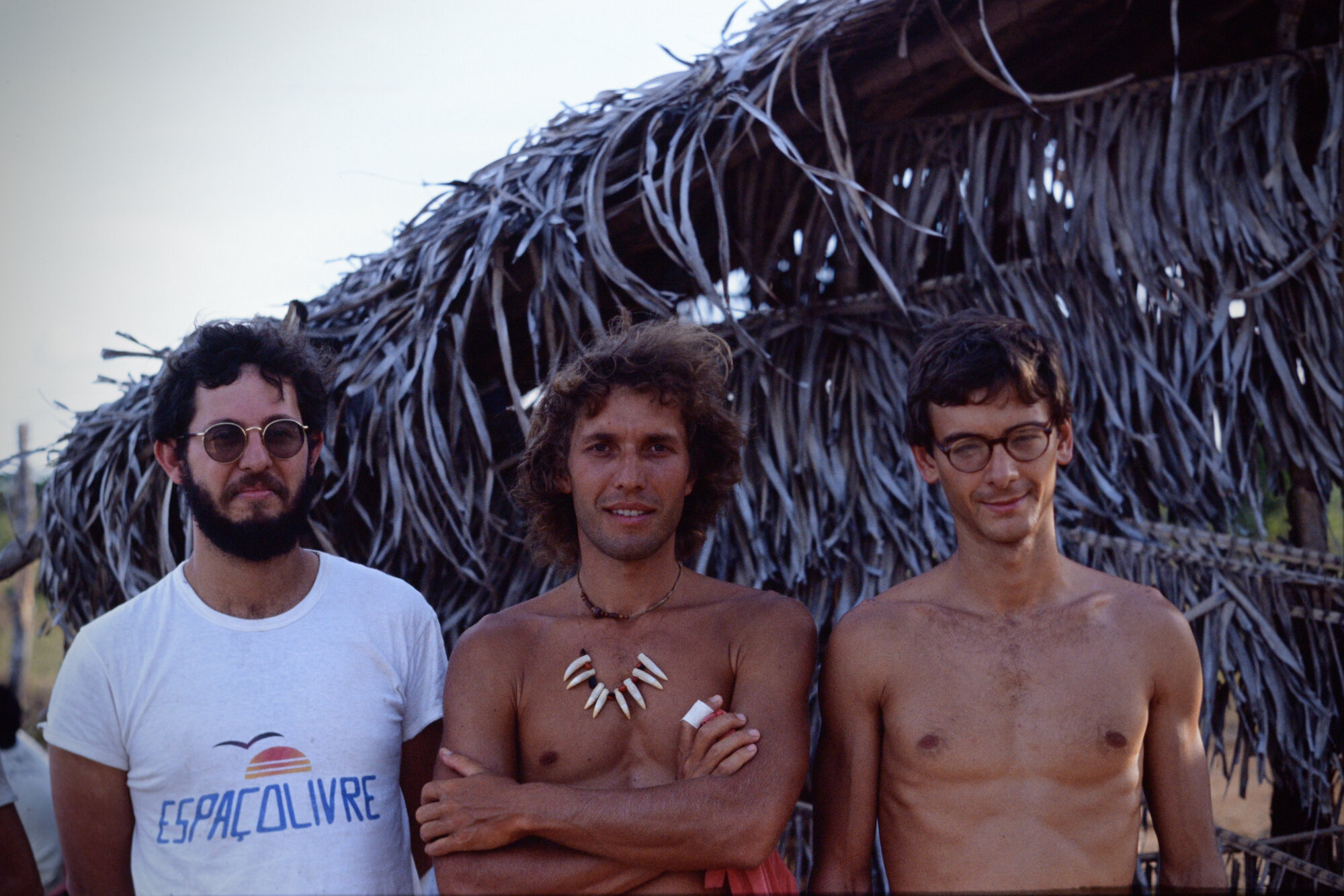 Three young researchers standing together in front of a thatched palm roof structure
